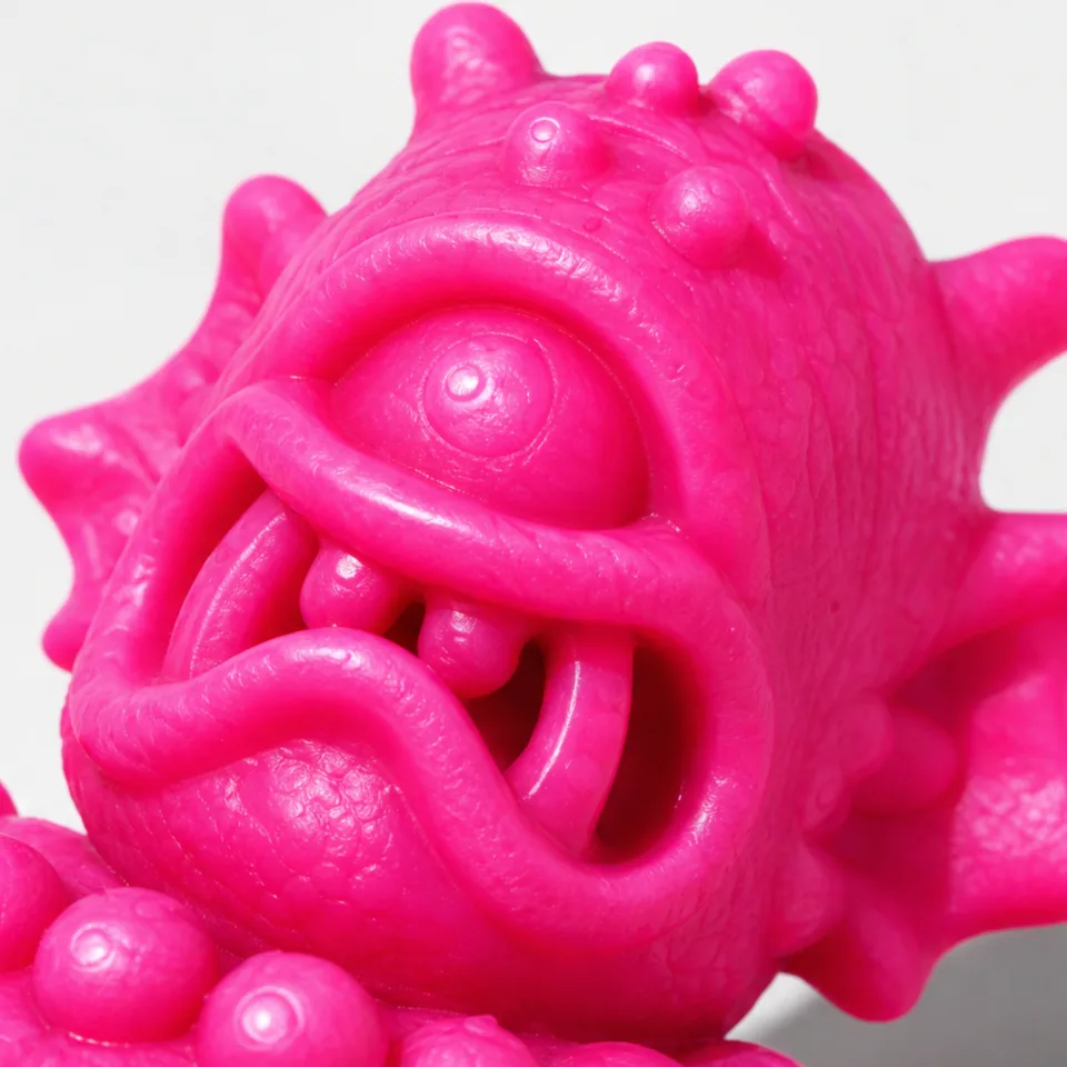 Hot-pink close-up of the cyclops face: a domed eye with a raised iris and pupil, thick eyelids, and separate rounded teeth inside a curled lip.