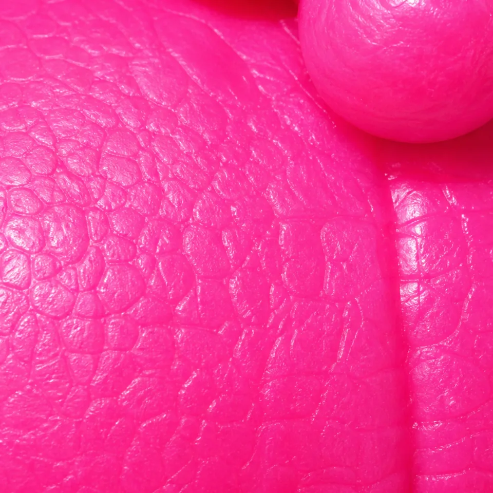 Hot-pink close-up of the figure’s surface, covered in a fine leathery grain of small irregular cells and creases.